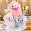 Trois peluches mignons en forme de mouton avec des cornes, un rose, un blanc et un bleu, portant tous un foulard rose à paillettes.