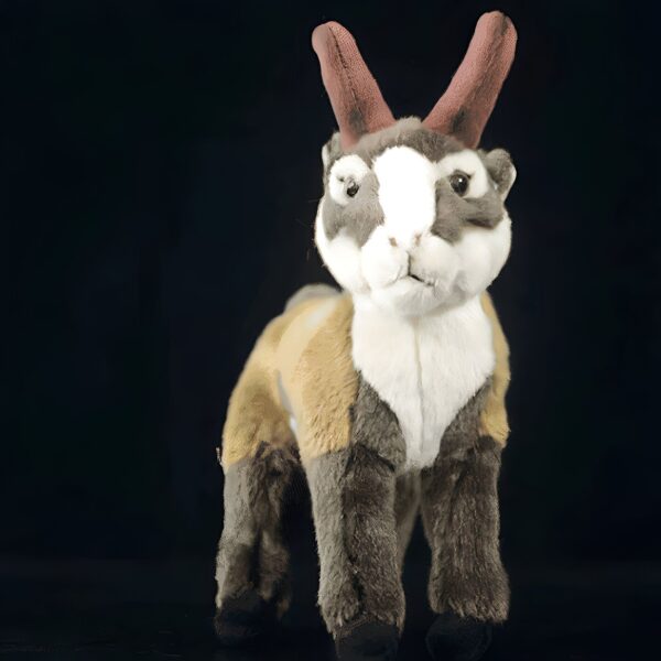 Une peluche de chamois en fourrure brune, blanche et jaune, avec de grandes cornes brunes, debout sur un fond noir.