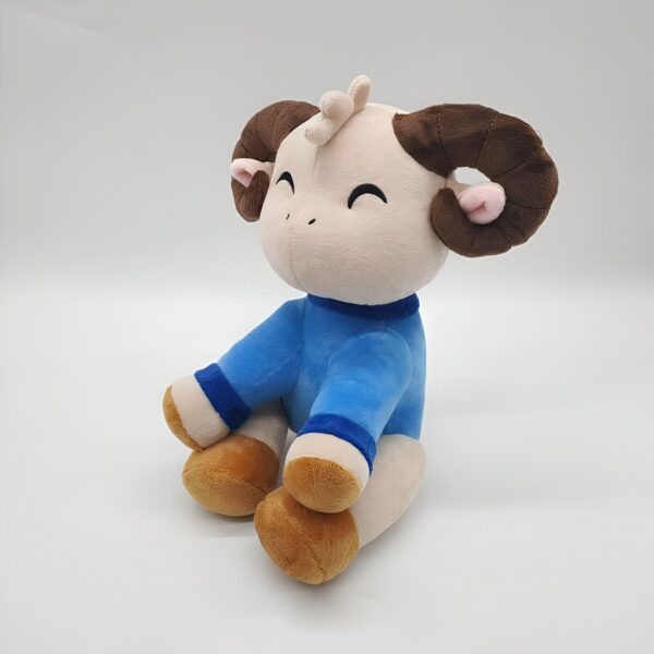 Une peluche mignonne en forme de mouton avec des cornes brunes, portant un pull bleu.