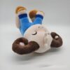 Peluche de mouton mignon portant un pantalon bleu, allongé sur le dos.