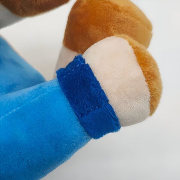 Gros plan sur le poignet d'un jouet en peluche avec un bracelet bleu. La main de la peluche est en fourrure blanche et brune.