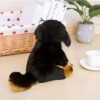 Un chien en peluche noir et marron assis sur un sol en bois.