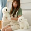 Une jeune femme assise sur un canapé blanc tient deux peluches de chiens blancs.