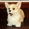 Une peluche de chien corgi à poil roux et blanc avec un sourire joyeux assis sur un piano.