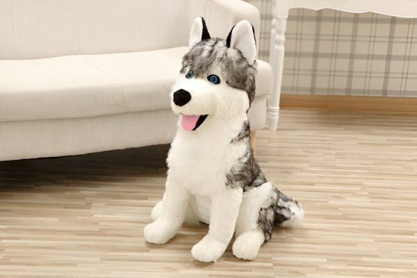 Un gros chien en peluche gris et blanc assis sur un sol en bois. Il a de grands yeux bleus et une langue rose qui dépasse.