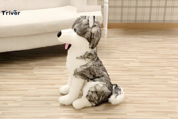 Un gros chien en peluche gris et blanc assis sur un plancher en bois.