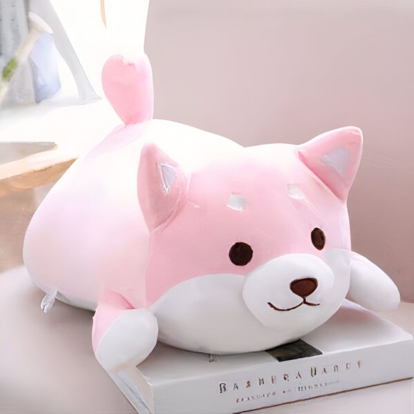 peluche-chien-japonais-kawaii-rose-jouet-en-peluche-pour-bebe-compagnon-calin-1a Peluche rose en forme de chien couché sur un livre.