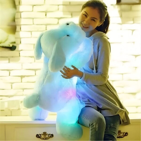 Une jeune femme souriante tient une grande peluche bleue qui s'illumine de différentes couleurs.