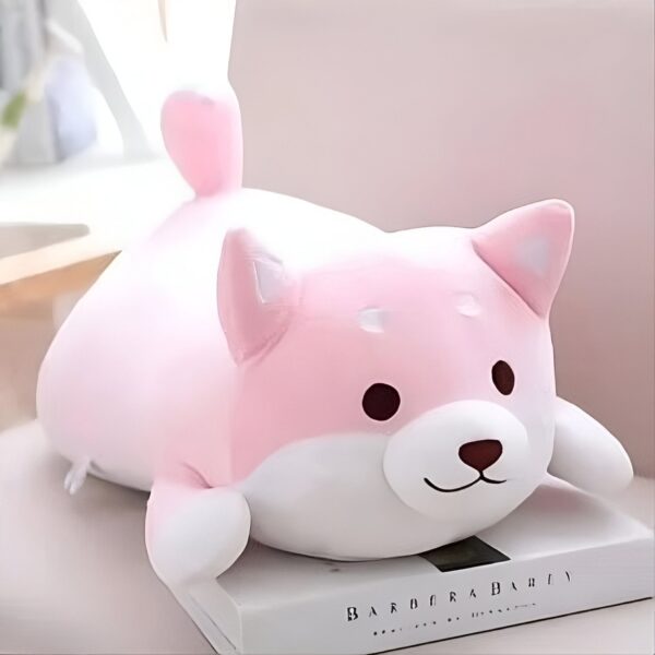peluche-chien-rose-japonais-peluche-doudou-bebe-jouet-enfant-2a Peluche rose en forme de chien couché sur un livre.
