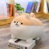 Une peluche en forme de chien Shiba Inu, de couleur beige et blanche, est posée sur un livre.