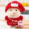 Peluche cochon souriant portant un bonnet rouge avec des lunettes rondes, un pull rouge "Je t'aime" et un petit sac rose.