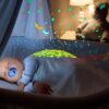 peluche-cochon-projecteur-etoiles-musique-bebe-sommeil-2a Bébé dort paisiblement dans son berceau, enveloppé de lumières et de musique apaisantes. Il est allongé sur un coussin lumineux projetant des étoiles colorées sur le plafond.