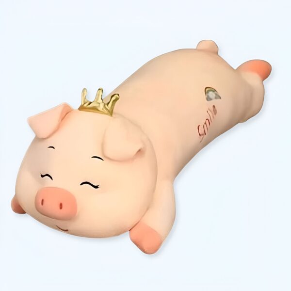 Un cochon rose en peluche portant une couronne dorée, dormant sur le ventre avec le mot "Smile" écrit sur son dos.