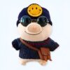 peluche-cochon-smiley-bonnet-et-lunettes-de-soleil-1a-3 Un cochon en peluche portant un chapeau bleu avec un smiley jaune, des lunettes de soleil rondes et un pull bleu avec une sacoche marron.