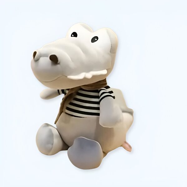 Jolie peluche de crocodile gris portant un t-shirt à rayures noires et blanches et une écharpe marron.