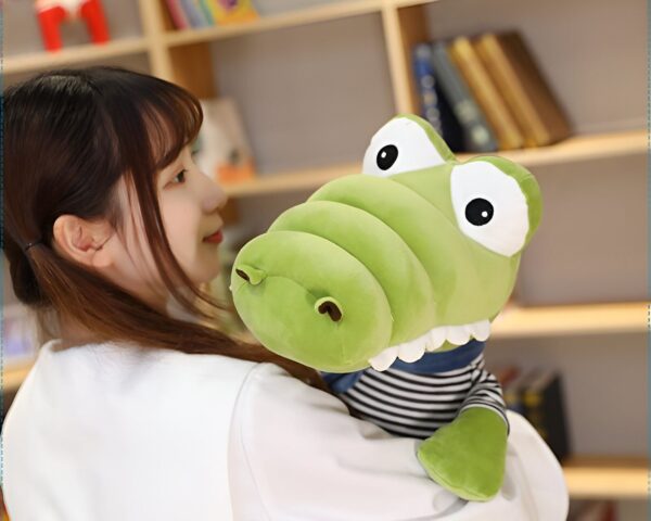 Une jeune femme tenant un grand crocodile en peluche vert portant un vêtement rayé bleu et blanc.