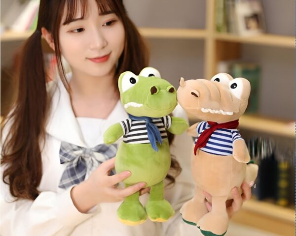 peluche-crocodile-bebe-marin-jouet-doux-enfant-2a Une jeune femme tenant deux peluches de crocodile, un vert et un beige, portant des vêtements rayés.