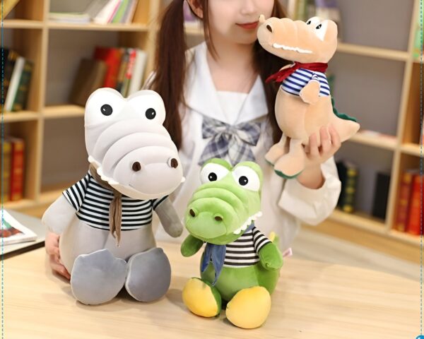 peluche-crocodile-bebe-marin-jouet-doux-enfant-3a Trois crocodiles en peluche, un gris avec un foulard rayé, un vert avec un foulard bleu et blanc et un beige avec un foulard rouge et bleu.