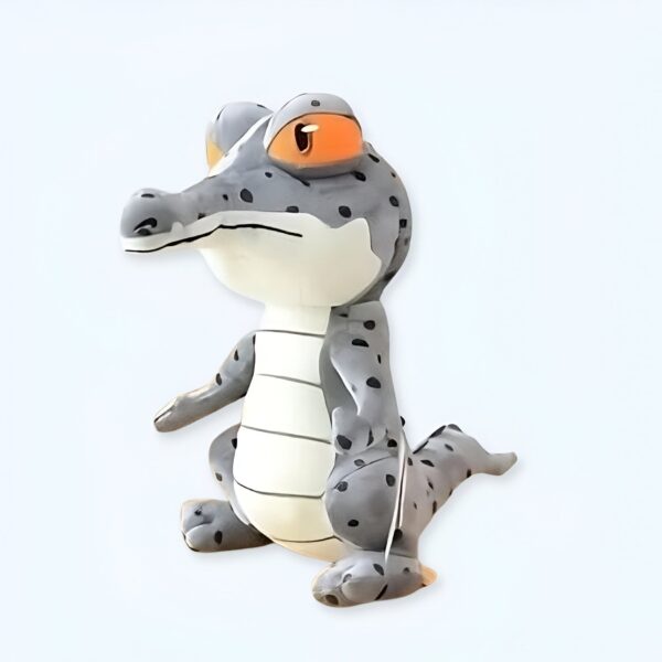 Une peluche de crocodile gris avec des points noirs et un œil orange.