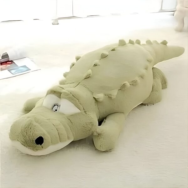 Gros coussin en forme de crocodile vert clair allongé sur un fond blanc.