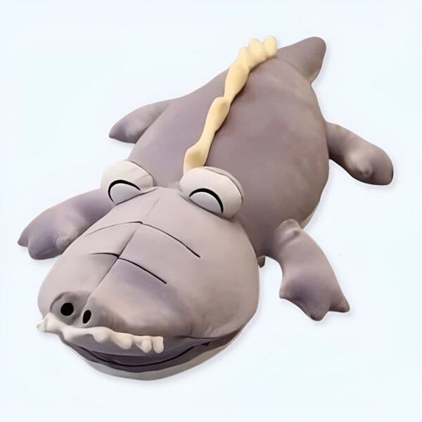 Un gros coussin en forme de crocodile gris avec une crête jaune sur le dos. Il a de grands yeux et une bouche ouverte avec des dents.