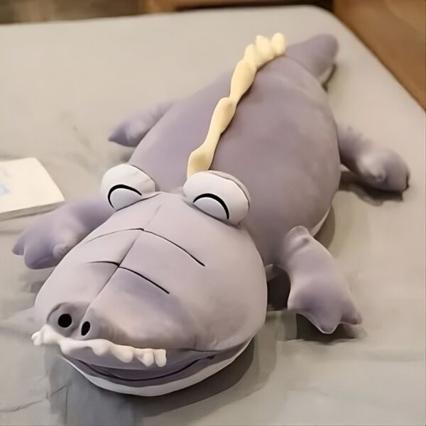 Gros coussin en forme de crocodile gris avec des yeux et des dents brodés. Parfait pour décorer une chambre d'enfant.