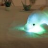 peluche-dauphin-lumineuse-lampe-de-chevet-et-compagnon-de-sommeil-1a-1 Un dauphin en peluche blanc lumineux vert sur une table blanche.