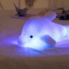peluche-dauphin-lumineuse-lampe-de-chevet-et-compagnon-de-sommeil-3a Une peluche de dauphin blanc lumineux sur un lit blanc.