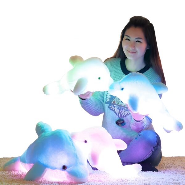 peluche-dauphin-lumineuse-lampe-de-chevet-et-compagnon-de-sommeil-4a Une jeune femme souriante tenant trois peluches dauphins lumineux de différentes couleurs.