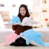 peluche-dauphin-lumineuse-lampe-de-chevet-et-compagnon-de-sommeil-5a Une jeune femme souriante tient trois peluches dauphins, un bleu clair, un blanc et un rose. Les dauphins sont doux et moelleux.