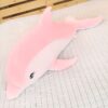 Une grande peluche rose en forme de dauphin sur un lit blanc à motifs.