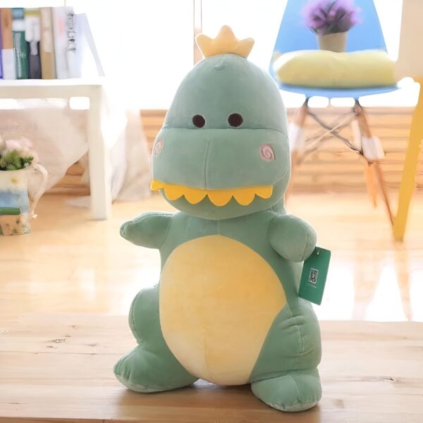 peluche-dinosaure-amusant-jouet-doux-pour-enfant-4a-5 Une peluche verte en forme de dinosaure avec une couronne jaune sur la tête, debout sur un plancher en bois.