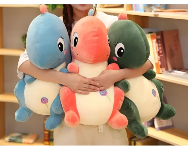 Une femme tient trois peluches en forme de dinosaure : un bleu, un orange et un vert.