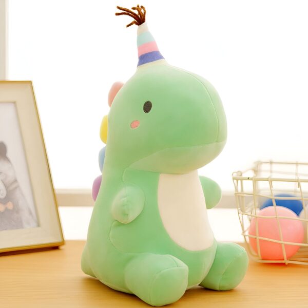 Peluche de dinosaure vert avec un chapeau arc-en-ciel assis sur une table en bois.