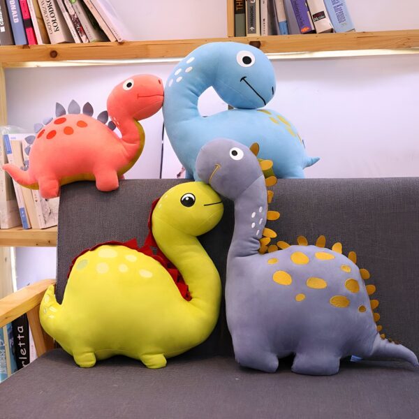 Quatre coussins en forme de dinosaure. Un bleu, un jaune, un gris et un rose. Ils sont tous disposés sur un canapé gris.
