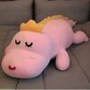 Gros ours en peluche rose avec des yeux noirs et une crête dorée allongé sur un lit gris.