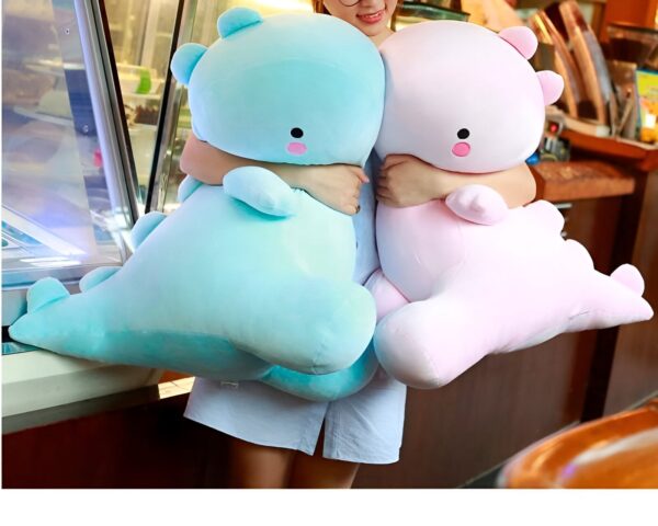 peluche-dinosaure-rose-jouet-doux-et-calin-pour-enfants-2a Une jeune femme tenant deux peluches en forme de dinosaure, l'une bleue et l'autre rose.