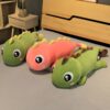 Trois dinosaures en peluche, un vert, un rose et un autre vert, posés sur un lit.