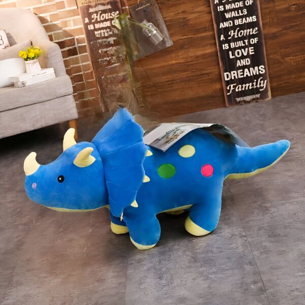 peluche-dinosaure-toute-douce-bleue-3a Peluche bleu de tricératops avec des points jaunes, verts et rouges, assis sur un sol en bois.
