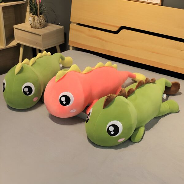 Trois peluches en forme de dinosaure, une verte, une rose et une verte, sont couchées sur un lit.