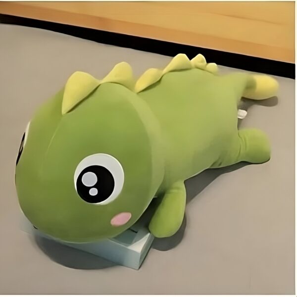 Peluche de dinosaure vert avec de grands yeux noirs et des joues roses. Il est allongé sur le dos.