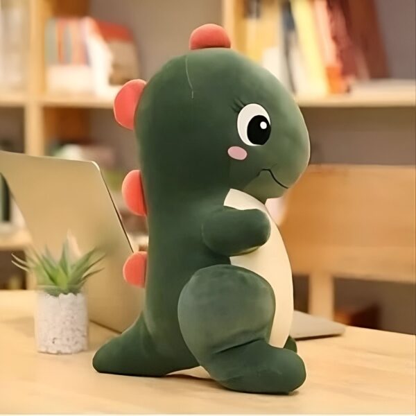 Peluche de dinosaure vert avec des détails roses sur un fond en bois.