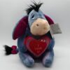 Une peluche bleu représentant l'âne Winnie l'ourson tenant un cœur rouge avec l'inscription "Je t'aime".