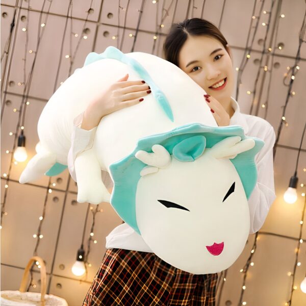 Une jeune femme sourit en tenant une grande peluche blanche avec des détails bleus et des yeux noirs.