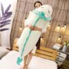 Une jeune femme souriante tenant une grande peluche blanche en forme de dragon avec des ailes turquoise.