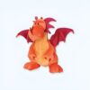Peluche de dragon orange avec des ailes roses, debout sur un fond blanc.