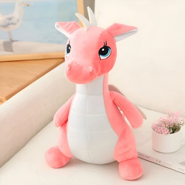 peluche-dragon-rose-mignon-jouet-doux-et-calin-pour-enfant-1a-4 Peluche de dragon rose avec des yeux bleus, debout sur un fond blanc.