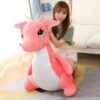 Une jeune femme souriante assise sur un grand dragon rose en peluche.