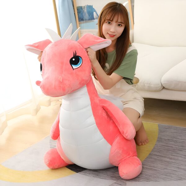 Une jeune femme souriante assise sur un grand dragon rose en peluche.