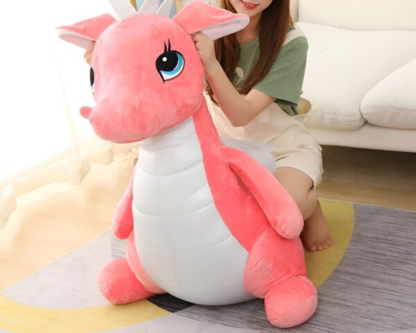 Une femme assise sur un canapé avec une grande peluche rose en forme de dragon.